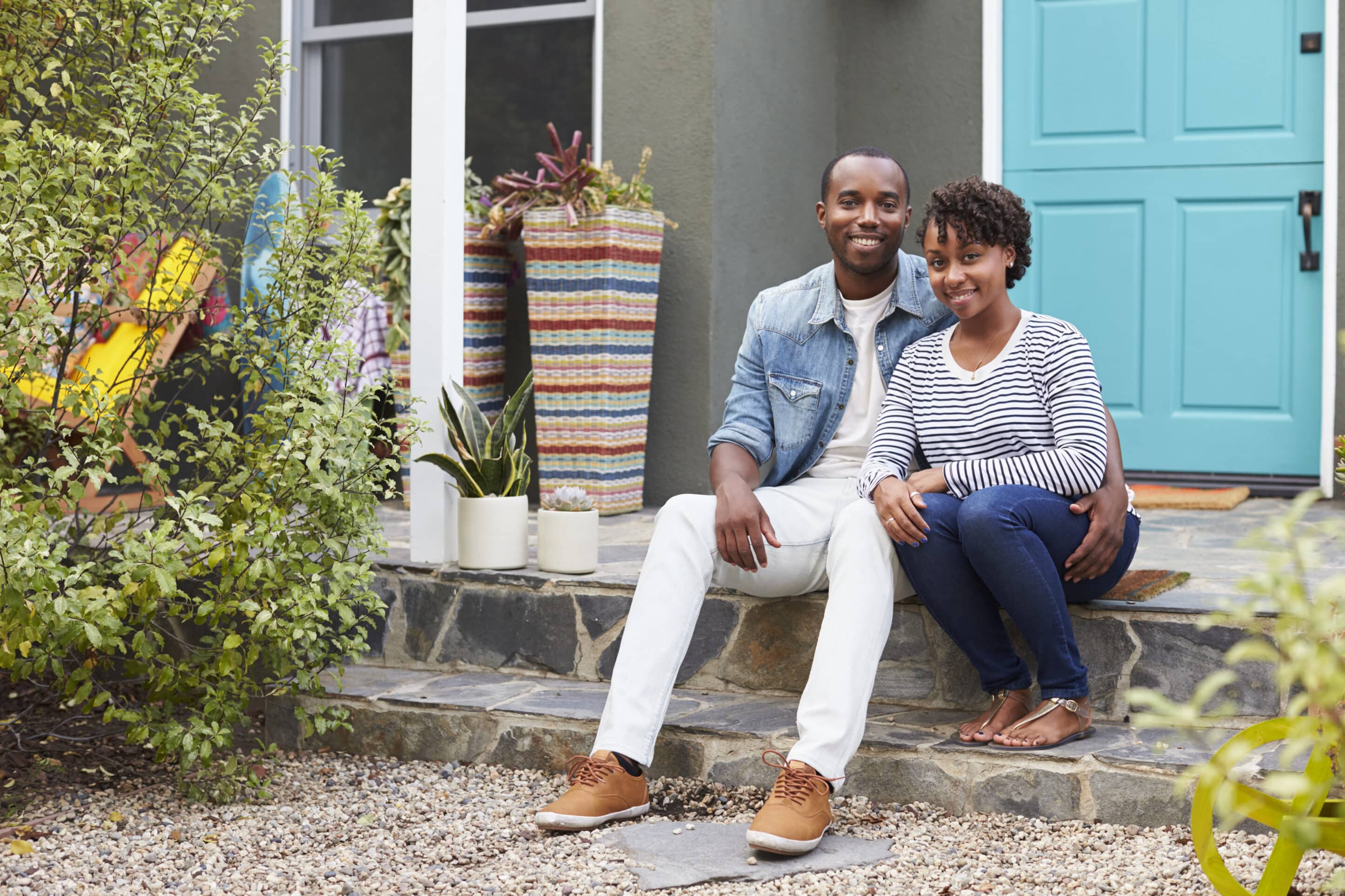 Young couple sit looking to camera outside their new house Young couple on porch